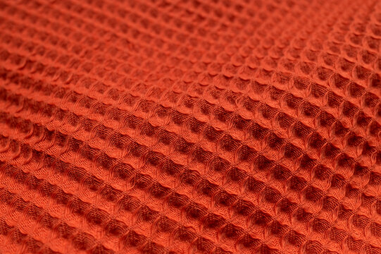 Orange cotton fabric forms textured background with soft folds. Waffle cloth, woven surface, and tactile textile detail offer versatile visual space for autumn campaigns, crafts, and home styling.