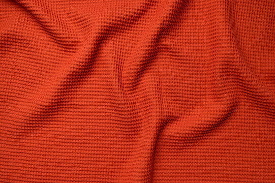 Orange waffle fabric fills frame, showing cotton texture with soft folds. Textile surface, woven material, and tactile structure create useful background for autumn branding and product design.