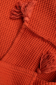 Red orange blanket displays textured weave, decorative tassels in closeup. Textile soft material, cozy fabric detail, home decor, and retail, woven waffle texture. Cotton blanket mockup