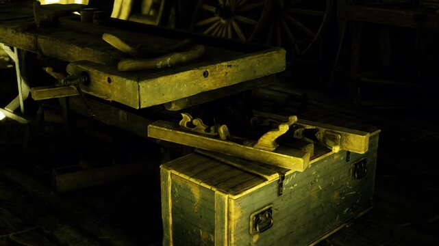 Angled view of open tool chest filled with planes and wood shavings, warm light spilling onto floor and boards, handles and hardware catching highlights,