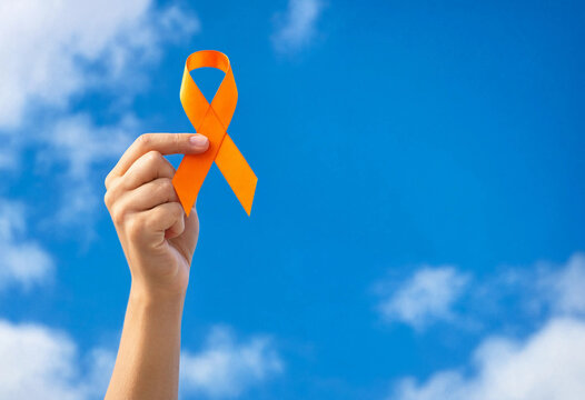 A hand holding an orange awareness ribbon up against a clear bright blue sky representing solidarity and support for important social causes
