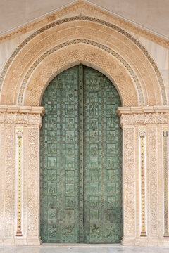 Ornate bronze arched door on an Arab-Norman cathedral facade,