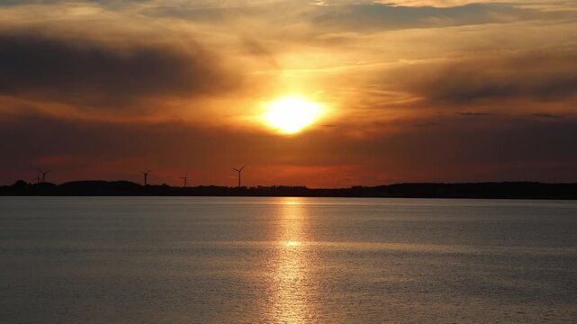 Golden sun setting over the calm water and wind turbines