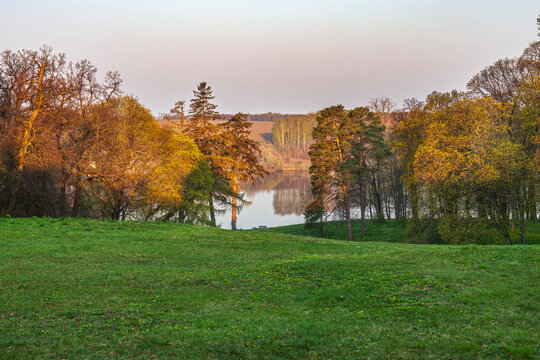 Beautiful scenic view of a spring park with green lawn and forest lake at sunset