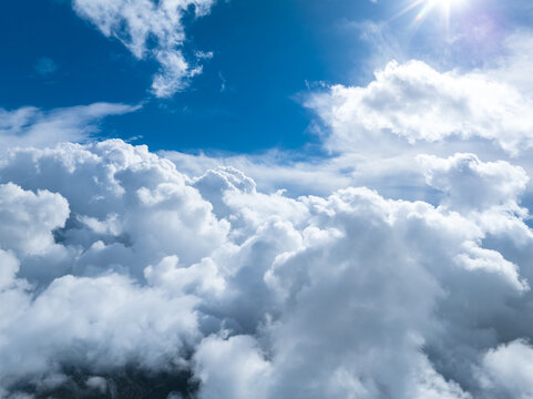 Aerial view of dense white cumulus clouds under a bright blue sky with a sun flare in France.