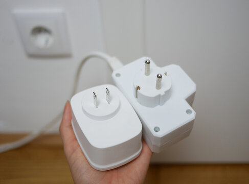 Two types of socket plugs - European round-pin plug and American flat-pin plug. Universal travel adapter in a hand close up. Electric plug adapter, international plug socket gadget for travel.