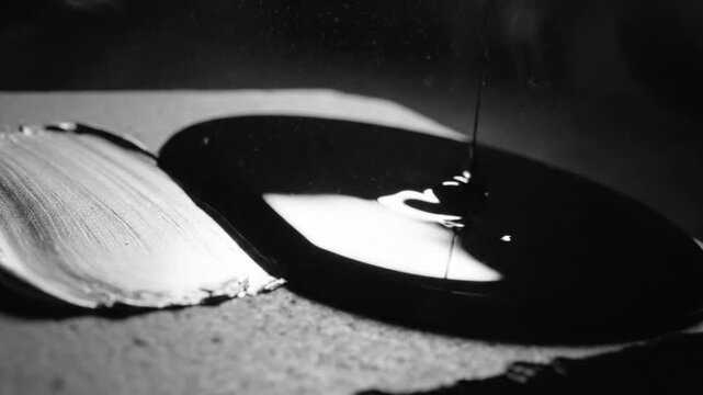 Black and white artwork composition revealing a painterly brushstroke and pouring of dark liquid, abstract concept.