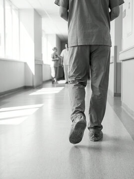Monochrome nurse walking away with strong shadows across a tiled floor