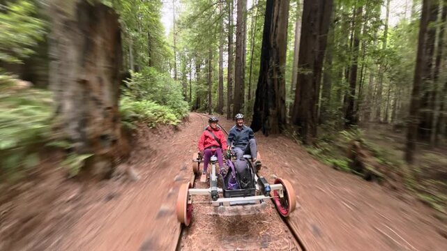 Mature couple enjoys an electric railbike ride along old railroad tracks in a forest of redwood trees near Fort Bragg California.
