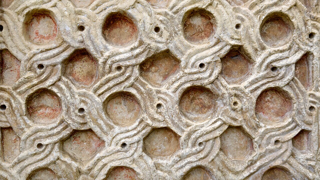 Ancient stone relief with intricate geometric waves, interlocking circles and hexagons, weathered surface and small erosion holes  detailed architectural texture, full frame close up