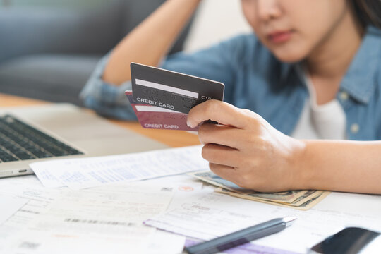 Financial owe, stressed asian woman, girl hand holding credit card, stressed by calculate expense from invoice or bill, no money to pay, mortgage or loan on table at home. Debt, bankruptcy or bankrupt
