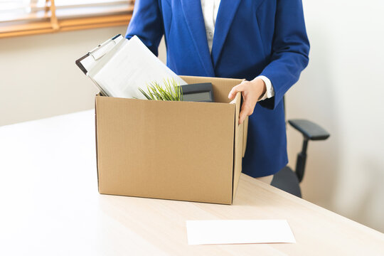 Unemployed, quite job. Desperate asian young businesswoman resigning from company, hand holding cardboard, packing belongings, stuff into box, layoff or changing work. Resignation, employment concept.