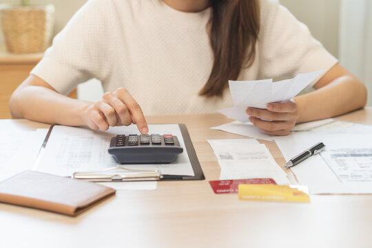 Stressed asian young business woman, employee using calculator to calculate expenses of monthly, hand holding bills and receipt for to payment on table at home. Financial, finance of banking concept.