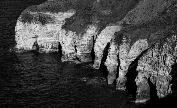 High-contrast black and white view of dramatic chalk cliffs and sea caves shaped by coastal erosion at Flamborough Head on the Yorkshire coast, England.