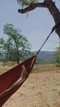 Relaxing hammock swing surrounded by mountains and trees
Close view of feet gently moving while swinging in a hammock outdoors, surrounded by green trees and mountain scenery. Peaceful relaxation 