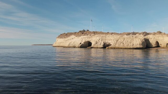 Coastal cliff landscape with sea caves and calm ocean water at sunset.