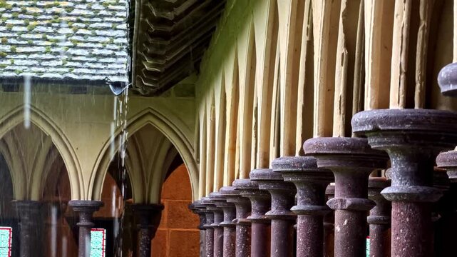 Rain falling from ancient stone arches in gothic cloister walkway with row of pillars.