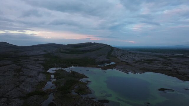Aerial view of Burren limestone landscape and coastal lake at twilight with pink clouds and rugged terrain in Ireland.