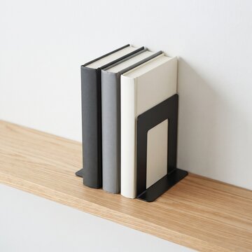 Minimalist black metal bookends on wooden shelf, modern home office decor, three hardcover books in neutral tones