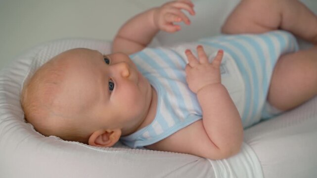 Active baby secured in soft baby nest looking around. Close-up.
