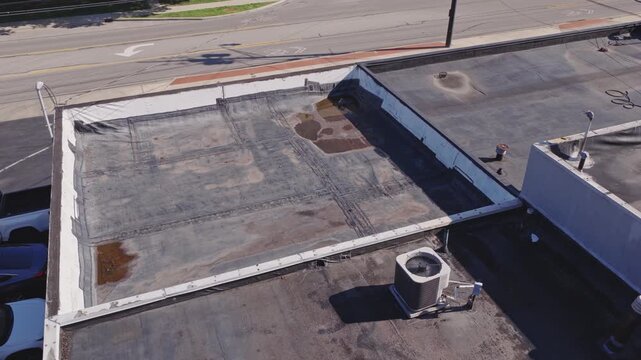 Aerial drone view above flat industrial retail business building rooftop and even roof with canvas having water damage from heavy rain and rainfall causing leaks and tears on roof's top with flooding