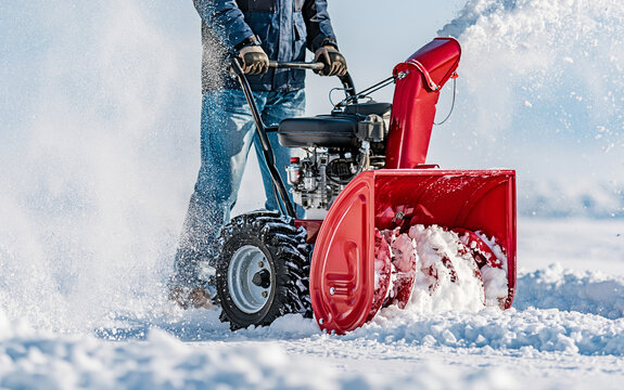 Person operating red snow blower to clear snow from driveway in winter