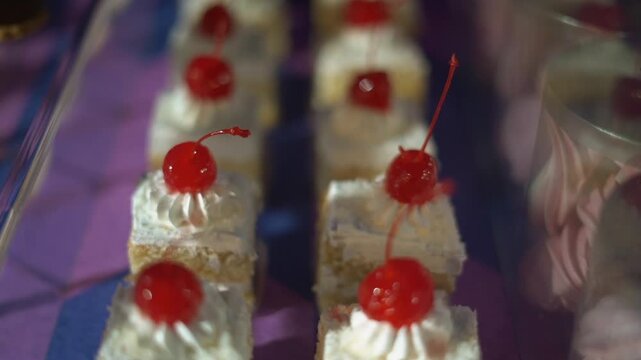 Mini vanilla cakes topped with whipped cream and maraschino cherries on dessert table display, rack focus close up