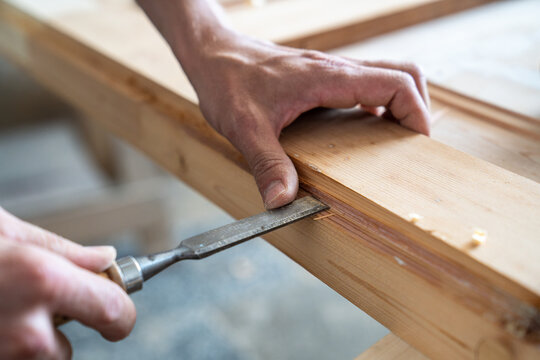Master deeply carving surface of antique wooden door at workbench in carpentry with chisel tool, talented craftsman cutting removing wood layers from groove, accuracy and skills in restoration craft.