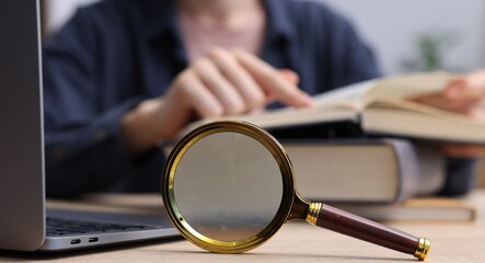 Fototapeta premium Keywords. Woman with magnifying glass, books and laptop at table, selective focus