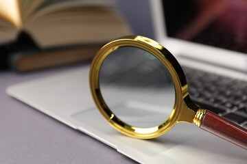 Fototapeta premium Keywords. Magnifying glass, laptop and books on grey background, selective focus