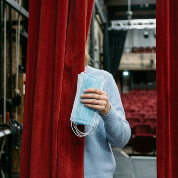 Person behind red curtains holding a stack of disposable face masks indoors