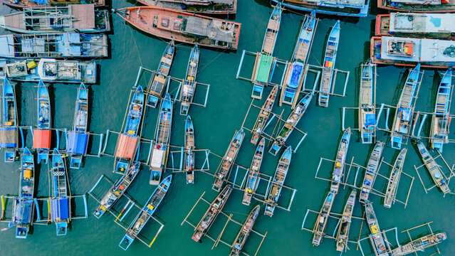 Aerial view of numerous colorful traditional fishing boats moored in the harbor with calm blue water in Palabuhanratu, West Java, Indonesia.