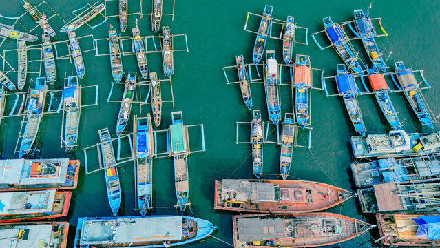 Aerial view of colorful traditional fishing boats moored in the harbor with calm turquoise water in Palabuhanratu, West Java, Indonesia.