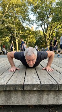 Older man performing push-ups on outdoor wooden platform, aging gracefully concept