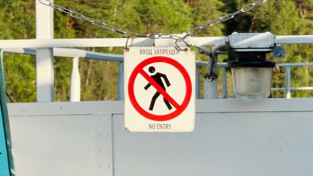 A no entry sign hangs on a chain aboard a cruise ship deck. It protects restricted areas as the ship sails past lush green shores. Travelers feel calm and safe on Lake Ladoga.