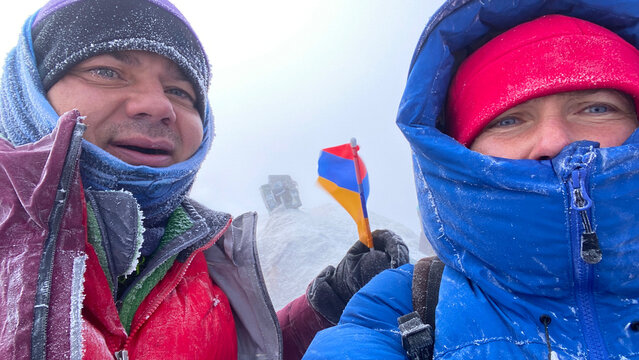 Climbers documenting summit arrival in close-up on Mount Ararat, Turkey, during a blizzard with frozen clothing