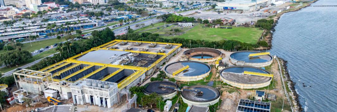 Aerial view of the wastewater treatment plant with circular clarifiers, biological treatment tanks, and sludge processing facilities along the coast in Florianopolis, Santa Catarina, Brazil.