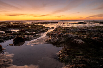 Obraz premium Tide Pool Channel Leading to Ocean at Golden Sunset on Rocky Beach, Coastal Seascape