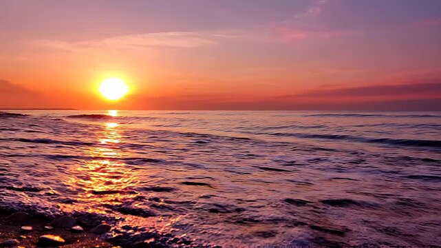 Ocean waves crashing on a sandy beach with pebbles at sunset