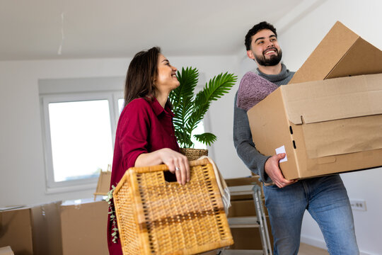 Couple carrying cardboard boxes and a wicker basket while moving home