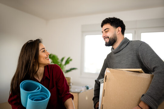 Couple talking while carrying moving boxes and rolled yoga mats at home