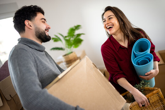 Couple laughing while carrying a cardboard box and rolled yoga mats