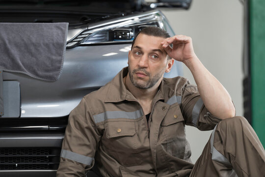 Stressed of man mechanic sitting on floor at services garage. Work delays, problems with the work, complain for work. Serious work