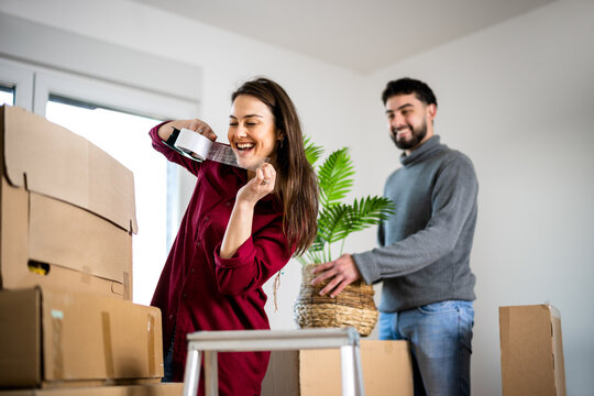 Woman drinking from a bottle while her partner moves boxes at home