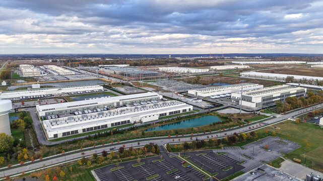Aerial view of a large industrial data center complex with modern white buildings, parking lots, and retention ponds under a cloudy sky in New Albany, Ohio, United States.