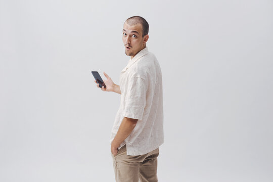 Surprised Young Man Holding Smartphone Looking Back Over Shoulder