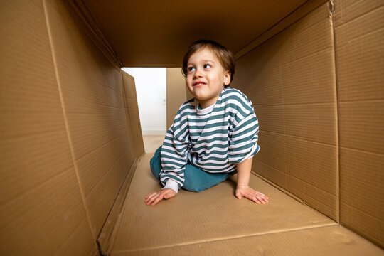 Young boy sitting inside a large cardboard box at home