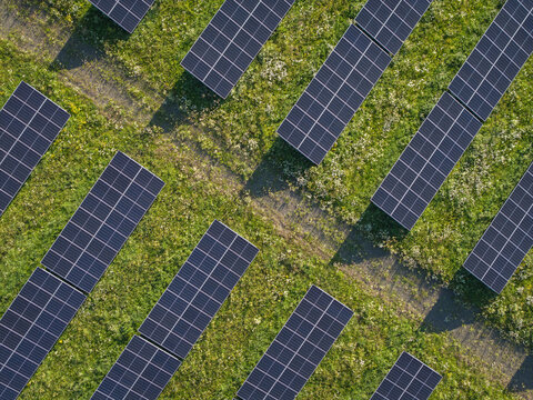 Aerial view of rows of solar panels installed in a green grassy field under bright sunlight in Poland.