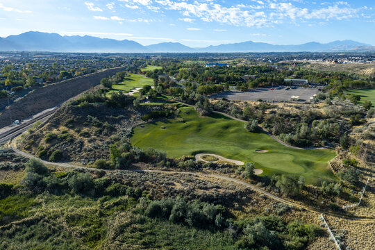 Aerial view of Thanksgiving Point Golf Course featuring lush green fairways, sand bunkers, and surrounding residential landscape under a clear blue sky in Lehi, Utah, United States.