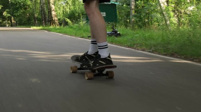 Person rides skateboard on a path surrounded by trees during daytime in a park
